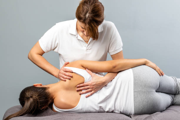 terapeuta mujer manipulando la lámina de hombro en paciente femenino joven. - chiropractic adjustment fotos fotografías e imágenes de stock