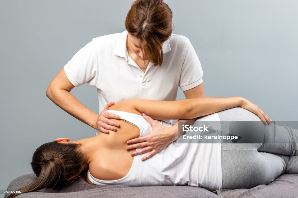 Female therapist manipulating shoulder blade on young female patient. Close up of female osteopath doing shoulder blade therapy on young woman. Osteopath Stock Photo