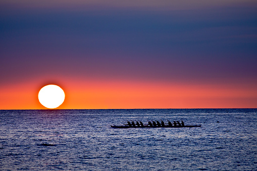 The outrigger canoe, a local boat vessel in the Hawaiian culture. An outrigger rowing along the ocean at Kailua-Kona at sunset.