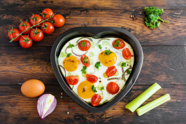 Romantic breakfast for Valentine day or anniversary, fried eggs with tomatoes, celery, onion and parsley in heart shaped baking dish. Rustic wooden table, fresh vegetables, ingredients for cooking. Top view. Romantic breakfast for Valentine day or anniversary, fried eggs with tomatoes, celery, onion and parsley in heart shaped baking dish. Rustic wooden table, fresh vegetables, ingredients for cooking. Top view. celery heart stock pictures, royalty-free photos & images