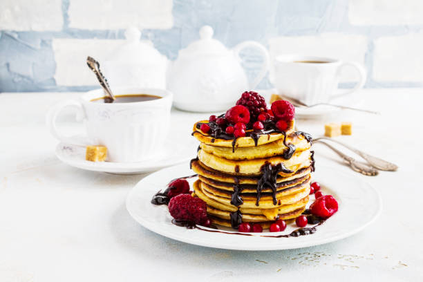 istock Stack of fried pancakes on a white plate. Chocolate, berries, raspberries, cranberries and blackberries on top. Gray concrete table, vintage forks, cup of tea with brown sugar, teapot. 698138466
