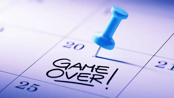 Concept image of a Calendar with a blue push pin. Closeup shot of a thumbtack attached. The words Game over written on a white notebook to remind you an important appointment.