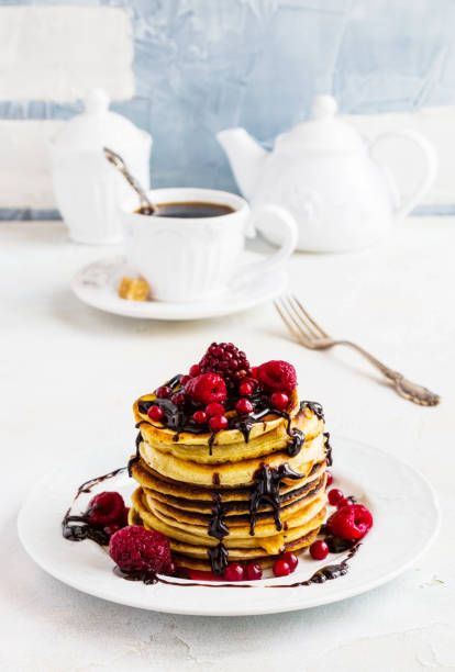 istock Stack of fried pancakes on a white plate. Chocolate, berries, raspberries, cranberries and blackberries on top. Gray concrete table, vintage forks, cup of tea with brown sugar, teapot. 698173286
