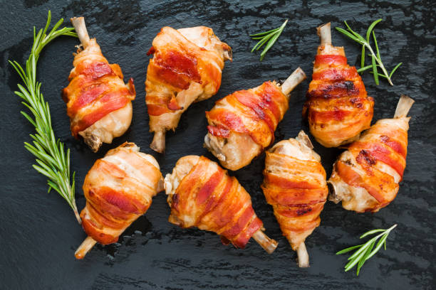 istock Bacon wrapped chicken drumsticks on a black stone background, top view. 698179662