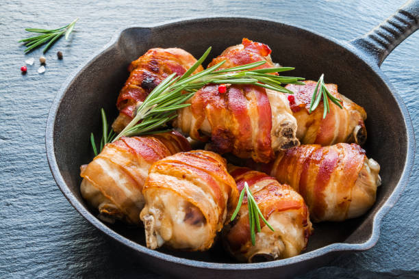 istock Bacon wrapped chicken drumsticks in a black cast-iron skillet on the stone background. 698184332