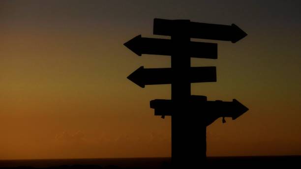 istock Silhouette of a post with arrows for directions at sunset 698189488
