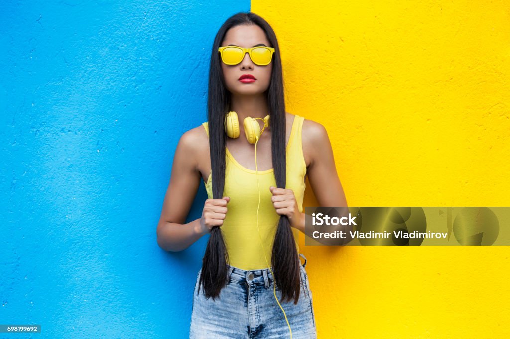 Woman in yellow vest,headphones and sunglasses Woman wearing yellow vest, vest and sunglasses in front of red and yellow background Fashion Model Stock Photo