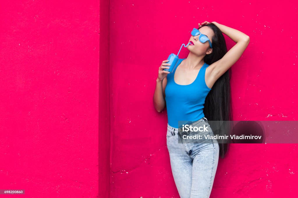 Woman in blue Woman in blue vest and sunglasses in front of pink wall background holding red can Long Hair Stock Photo