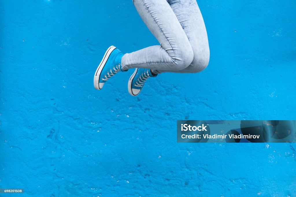 Woman legs in blue Jumping woman legs in blue sneakers against  blue wall background Jumping Stock Photo