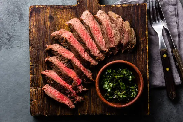 Photo of Mediun rare beef steak on wooden board. Top view