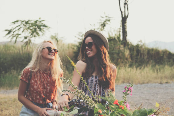 Two gilrs in boho clothes, and sunglasses pushing bike with flower basket