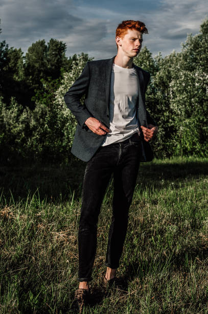 빨간 머리와 주 근 깨 자 켓을 입고 푸른 잔디에 서 매력적인 세련 된 젊은 남자 모델의 초상화. 유행 야외 샷입니다. - prepossessing 뉴스 사진 이미지