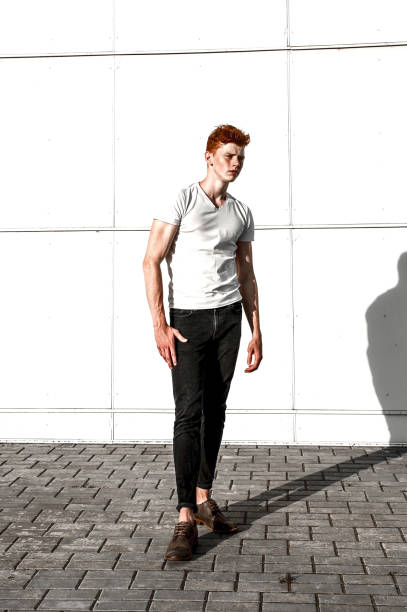 빨간 머리와 주 근 깨, 흰 t 셔츠를 입고 흰색 벽 근처 서 매력적인 세련 된 젊은 남자 모델의 초상화. 유행 야외 샷입니다. - prepossessing 뉴스 사진 이미지