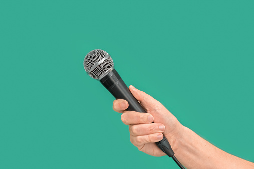 Interviewer or reporter with microphone in hand on green background, mic. Front view