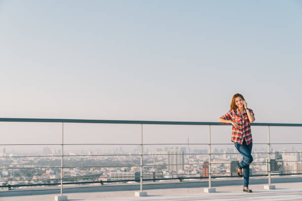 istock Beautiful Asian woman or college student using mobile phone call at rooftop during sunset, cityscape background. Communication, business, or education concept. With copy space 698286282