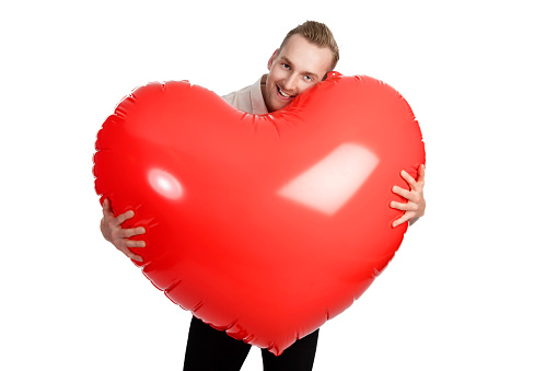 Man standing with a huge oversized heart with a big smile on his face wearing a white shirt. White background.