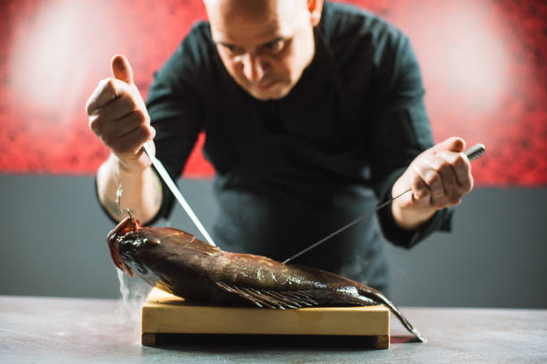 Chef cutting a big fish on a wooden board with two knives