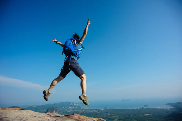 istock cheering woman hiker jumping on rocky mountain top 698338334
