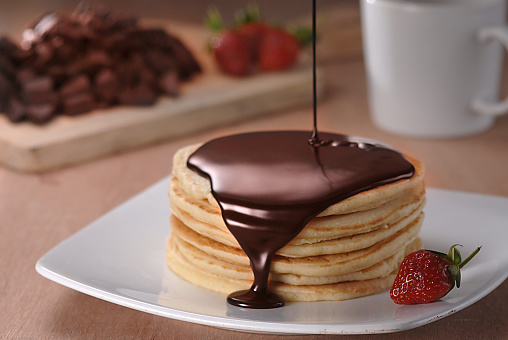 Chocolate syrup being poured over a stack of pancakes.