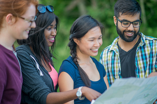 A serene looking group of multi-ethnic young people are looking at a map for directions during a nature hike at a campsite.