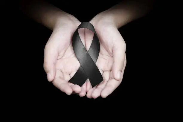 Photo of Hand holding black ribbon on black background mourning awareness sign