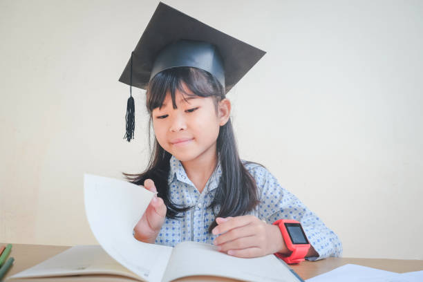 istock Asian school kid graduate in graduation cap and reading a book 698421158