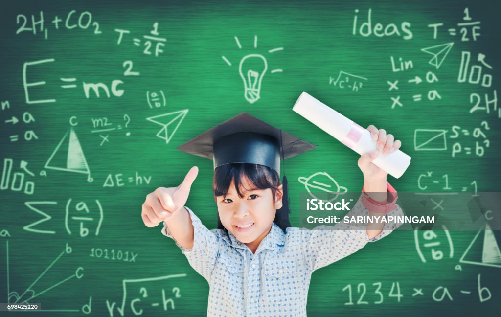 Asian school kid graduate in graduation cap for her success  over blackboard. Day Stock Photo