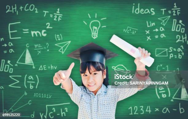 Asian School Kid Graduate In Graduation Cap For Her Success Over Blackboard Stock Photo - Download Image Now