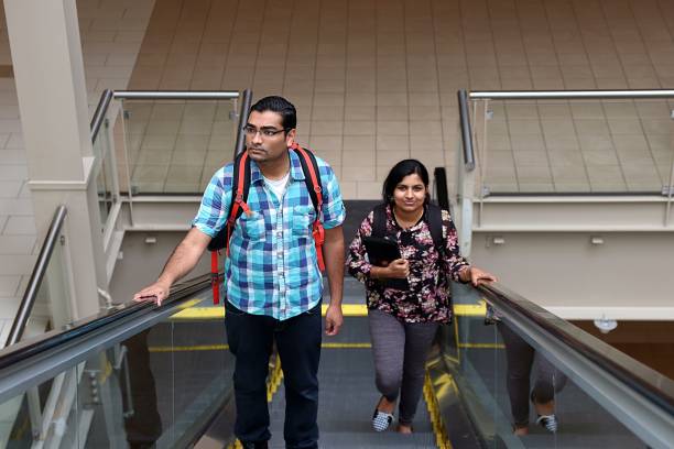 man and woman going up escalator Young attractive man and woman students going up escalator in industrial building, mall, airport india airport stock pictures, royalty-free photos & images