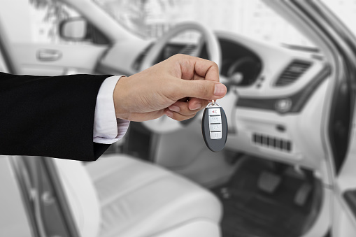 Hand holding car key remote, with modern car backgrounds