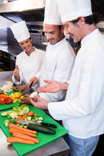 istock Head chef teaching his colleagues how to slice vegetables 698541372