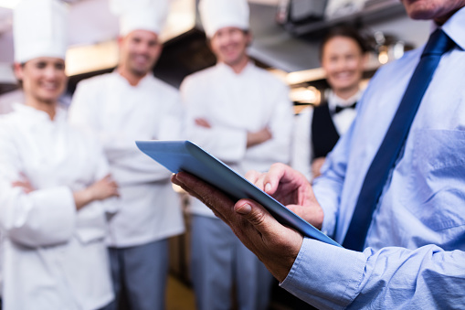Mid section of restaurant manager using digital tablet in commercial kitchen