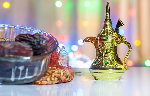 Golden Arabic Coffee Pot and date fruits in bowl with colorful background.