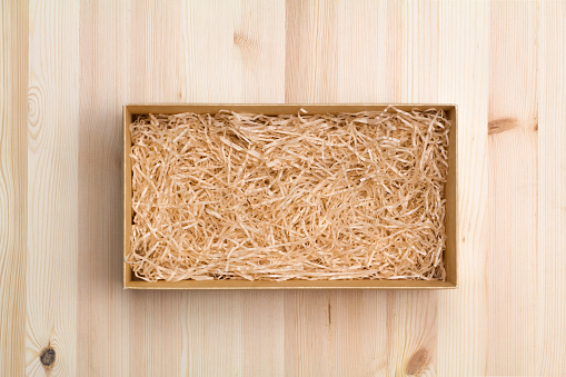 Gift box with decorative straw on wooden table, top view