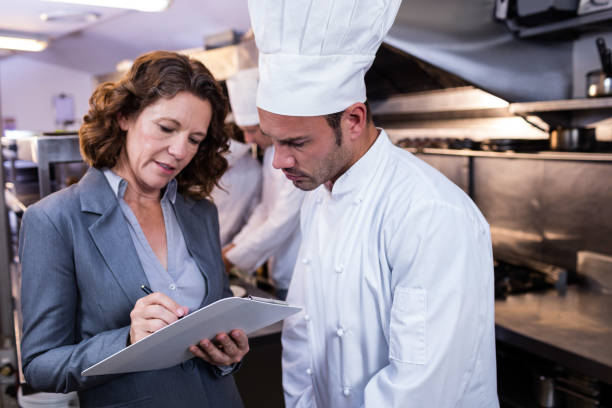 istock Female restaurant manager writing on clipboard while interacting to head chef 698582100