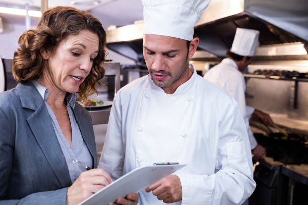 istock Female restaurant manager writing on clipboard while interacting to head chef 698582280