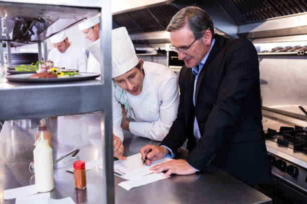istock Male restaurant manager writing on clipboard while interacting to head chef 698583190