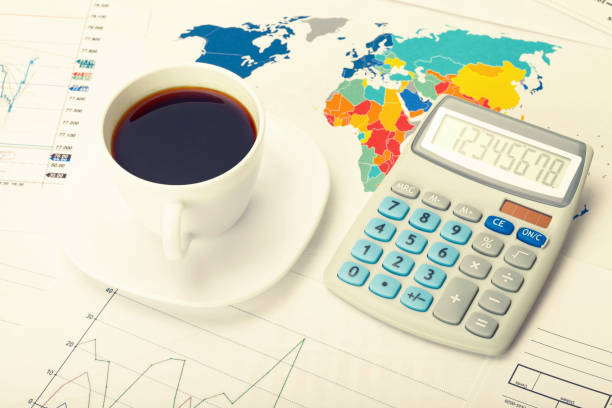 istock Coffee cup and calculator over world map and some financial charts. Filtered image: cross processed vintage effect. 698590542