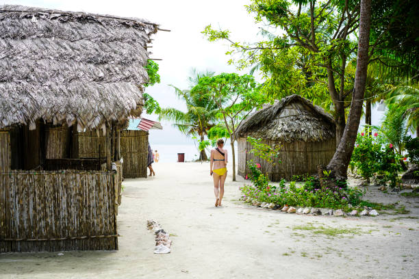 Senior woman in Kuna Yala turist village on island Naranjo Chico in Caribbean See Detail of Kuna Yala village with tourist cottages and senior woman walking on path. In front her is lokal market and some tourists on beach. It is on small  Island Naranjo Chico in San Blas archipelagos in Caribbean See, Panama.  Cottage is from wood, and bamboo.  San Blas is an old name for Panamas northeast province known for Kuna Yala indigenous people living there. Official they are Gunas and they live in Guna Yala province. The people are very small and mostly they don’t have connections with other people and cultures. kuna yala stock pictures, royalty-free photos & images