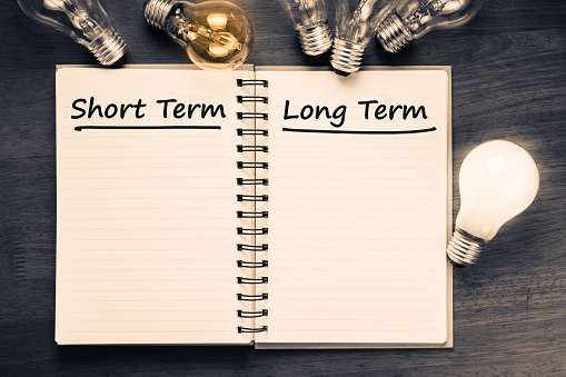 Short term and Long term on opened notebook with glowing light bulb