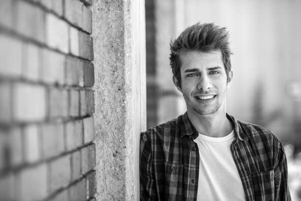 istock smiling young man leaning at brick wall 698615058