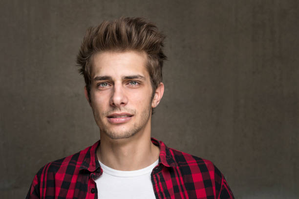 handsome young man looking at camera. He is wearing a checked red shirt with long sleeves.