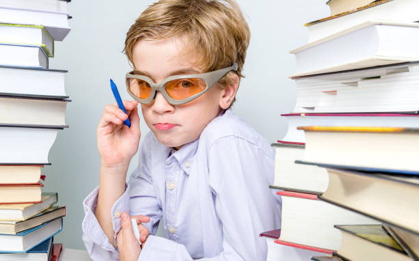 school boy with modern glasses learning between piles of books - child prodigy imagens e fotografias de stock