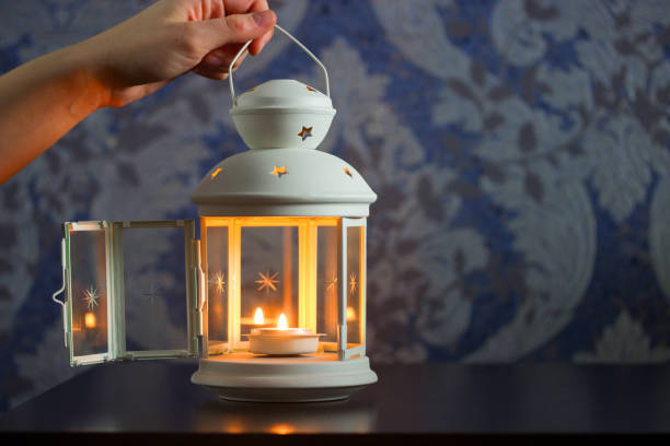 beautiful decoration lantern or candle holder of white iron and glass with star in female hand on brick wall background, copy space