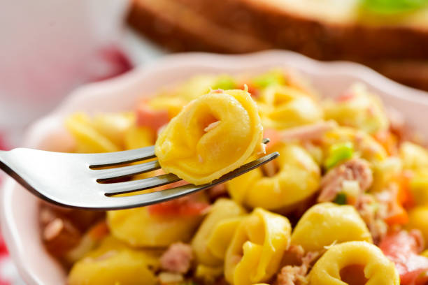 closeup of a ceramic bowl with a pasta salad made with tortellini on a table set for lunch or dinner