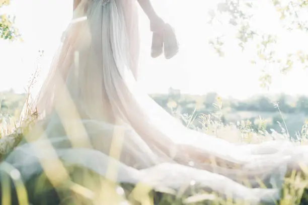 Photo of Bride in wedding dress holds shoes against sun. fine art photography