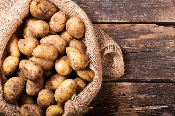 fresh potatoes in sack on wooden table stock photo