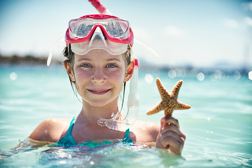 Little girl having fun snorkeling in beautiful sea. The girl is smiling at the camera and holding a star-fish. The girl is aged 8.
