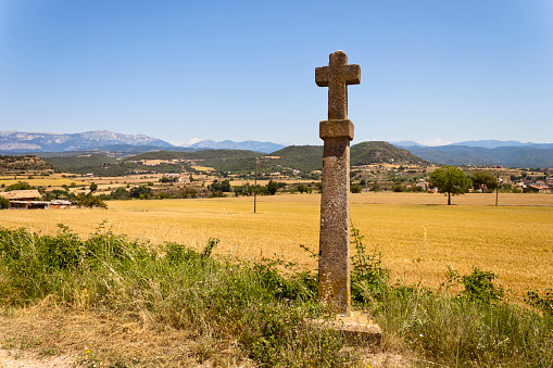 Stone croos in the Castellvell path in Solsona. Countryside summer landscape with Montsec range at background. Lleida, Catalonia, Spain.
