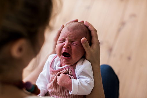 Unrecognizable young mother at home holding her crying newborn baby girl.